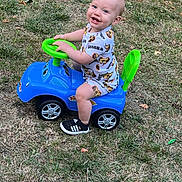 Thélyo participe au concours pour gagner de l'argent avec cette photo : toddler, child, toy_car, outdoor, grass, smiling, sitting, playtime, blue, green, shoes, shorts, shirt, person, cute, happy, summer, fun, young, play