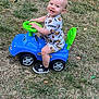 toddler, child, toy_car, outdoor, grass, smiling, sitting, playtime, blue, green, shoes, shorts, shirt, person, cute, happy, summer, fun, young, play