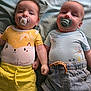 baby, infant, pacifier, bed, clothing, shorts, cute, face, lying_down, two_babies, child, adorable, toddler, yellow_shirt, blue_shirt, denim_shorts, soft_bed, holding_hands, closeup, indoors
