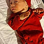 baby, newborn, infant, red_clothing, hat, blanket, bed, sleepwear, human, skin, face, hand, foot, cute, indoors, lying_down, small, portrait, child, cozy