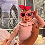 Sofia is registered to the contest to win money with this photo: baby, child, pink, sunglasses, heart_shaped_glasses, bow, holding, adult, arm, cityscape, skyscraper, gherkin_building, balcony, outdoor, sunny, fashion, cute, person, portrait, urban