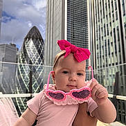 Sofia joined the competition — help win amazing prizes! baby, child, pink_bow, sunglasses, holding, urban, cityscape, skyscraper, outdoor, daylight, person, infant, cute, headband, building, modern, fashion, portrait, hand, sky