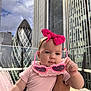 baby, child, pink_bow, sunglasses, holding, urban, cityscape, skyscraper, outdoor, daylight, person, infant, cute, headband, building, modern, fashion, portrait, hand, sky