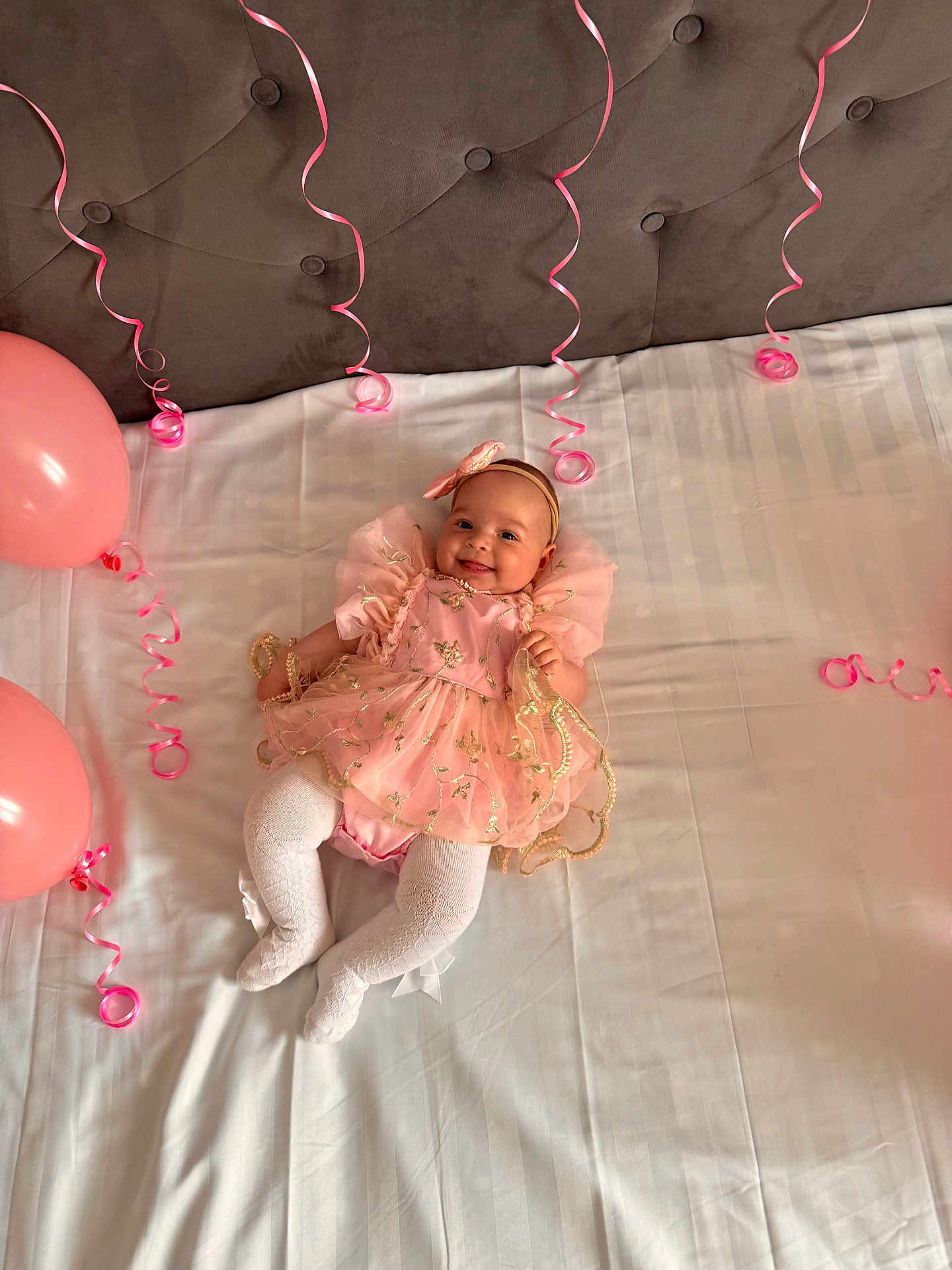 Sofia joined the competition — help win amazing prizes! baby, infant, pink_dress, white_tights, balloons, curly_ribbons, bed, smiling, headband, celebration, cute, child, portrait, indoors, soft_lighting, fabric, decorations, happy, small_person, toddler