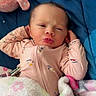 baby, bed, bedding, blanket, child, close_up, colorful, cozy, face, indoors, infant, lying_down, newborn, onesie, pillow, pink_clothing, portrait, pursed_lips, squinting, stuffed_animal