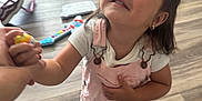 Mariella is registered to the contest to win money with this photo: barefoot, casual_clothing, child, cute, earrings, flooring, girl, holding_hand, home, indoor, interaction, looking_up, person, pink_overalls, play, short_sleeve, smiling, toy, wooden_floor, young_child