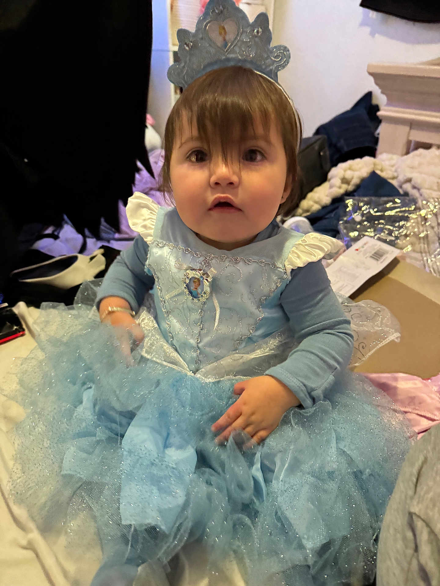 Mariella is registered to the contest to win money with this photo: toddler, child, dress, blue_dress, princess_costume, tiara, indoor, blanket, clothing, person, face, hair, sitting, curious, cute, soft_lighting, fabric, home, portrait, hands