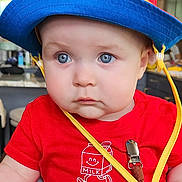 Kaden is registered to the contest to win money with this photo: baby, blue_eyes, child, clothing, colorful, curious_expression, cute, face, hat, high_chair, indoor, infant, milk_carton_graphic, person, portrait, red_shirt, seatbelt, sitting, striped_pants, young_child