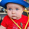 baby, blue_eyes, child, clothing, colorful, curious_expression, cute, face, hat, high_chair, indoor, infant, milk_carton_graphic, person, portrait, red_shirt, seatbelt, sitting, striped_pants, young_child