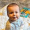 baby, book, carpet, child, colorful, cute, face, floor, homedecor, indoor, infant, pajamas, person, playtime, quilt, sitting, smile, soft, toy, young