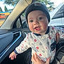 baby, beanie, car_interior, child, clothing, cute, face, hand, happy, holding, infant, inside, joyful, looking, mouth_open, outdoor_view, person, smiling, vehicle, window