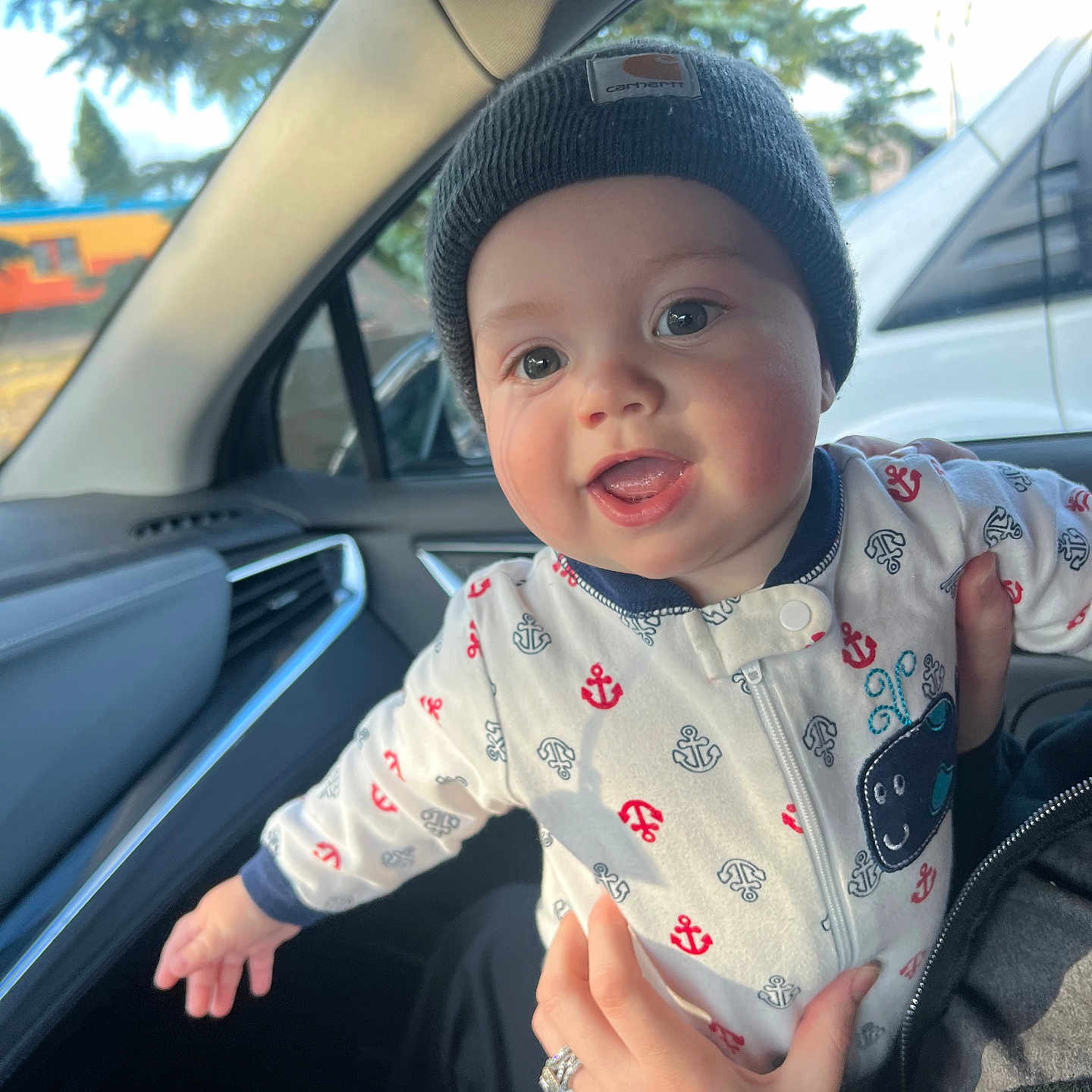 Bransen is registered to the contest to win money with this photo: baby, beanie, car_interior, child, clothing, cute, face, hand, happy, holding, infant, inside, joyful, looking, mouth_open, outdoor_view, person, smiling, vehicle, window