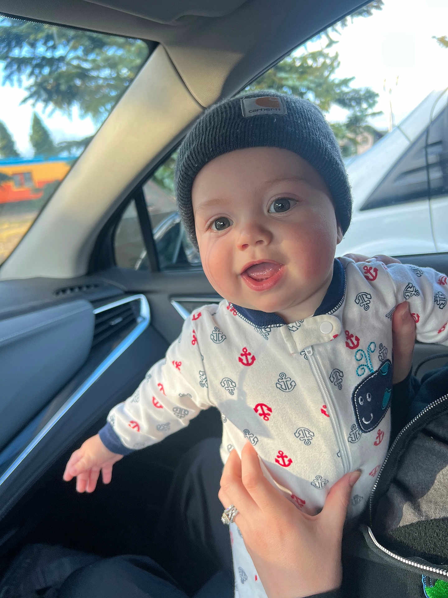 Bransen is registered to the contest to win money with this photo: baby, beanie, car_interior, child, clothing, cute, face, hand, happy, holding, infant, inside, joyful, looking, mouth_open, outdoor_view, person, smiling, vehicle, window
