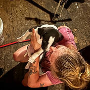 Gunner joined the competition — help win amazing prizes! person, puppy, dog, tattoo, indoor, wooden_floor, holding, black_and_white, short_sleeve, hair_tied, cute, pet, affection, kneeling, casual_clothing, animal, playing, young, friendly, love