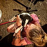 person, puppy, dog, tattoo, indoor, wooden_floor, holding, black_and_white, short_sleeve, hair_tied, cute, pet, affection, kneeling, casual_clothing, animal, playing, young, friendly, love