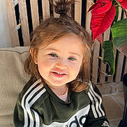 Sienna participe au concours pour gagner de l'argent avec cette photo : toddler, child, smiling, face, hair, topknot, adidas, tracksuit, clothing, sitting, cushion, chair, indoors, plant, poinsettia, string_lights, happy, portrait, young_child, casual