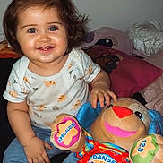 Sienna a rejoint le concours — aidez-le/la à gagner de superbes lots ! blanket, blue_jeans, child, colorful, curly_hair, cute, french_text, furniture, happy, indoor, person, pillow, playful, plush_toy, smiling, stuffed_animal, toddler, top_knot, toy, white_shirt