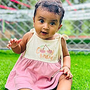 Ashlyn joined the competition — help win amazing prizes! baby, child, grass, outdoor, dress, cute, smiling, face, portrait, sitting, green, fence, person, happy, young_child, curly_hair, nature, summer, playful, eyes