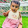 baby, child, grass, outdoor, dress, cute, smiling, face, portrait, sitting, green, fence, person, happy, young_child, curly_hair, nature, summer, playful, eyes