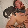 animal, arm_tattoo, bed, cat, close_up, facial_hair, gray_cat, human, indoor, man, nap, peaceful, pet, relaxation, resting, shirtless, shoulder, sleeping, tattoos, white_sheets
