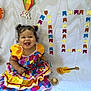 baby, celebration, child, colorful, corn, curly_hair, decorations, dress, fire, guitar, happy, hat, kite, number_10, paper_cutouts, portrait, puffed_sleeves, sitting, smiling, white_backdrop