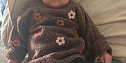 Lucianna participe au concours pour gagner de l'argent avec cette photo : baby, child, sweater, brown, flower_pattern, boots, bed, pillow, indoor, portrait, clothing, cute, young, infant, person, sitting, warm, cozy, footwear, looking