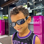 Aron participe au concours pour gagner de l'argent avec cette photo : child, boy, sunglasses, smile, curly_hair, earring, sleeveless_shirt, jersey, chicago, indoor, store, display_case, modern, lighting, fashion, portrait, casual, cool, person, shopping