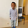 Aron participe au concours pour gagner de l'argent avec cette photo : child, boy, smiling, indoor, striped_shirt, jeans, blue_sneakers, wooden_floor, wall, power_outlet, heater, chair, earring, happy, standing, casual_clothing, curly_hair, home_interior, portrait, light