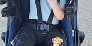 Rafael is registered to the contest to win money with this photo: baby, black_pants, blue_shirt, cartoon_lion, casual_clothing, child, cute, daylight, happy, infant, outdoor, pavement, person, portrait, safety_harness, seat, smiling, socks, straps, stroller
