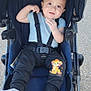 baby, black_pants, blue_shirt, cartoon_lion, casual_clothing, child, cute, daylight, happy, infant, outdoor, pavement, person, portrait, safety_harness, seat, smiling, socks, straps, stroller