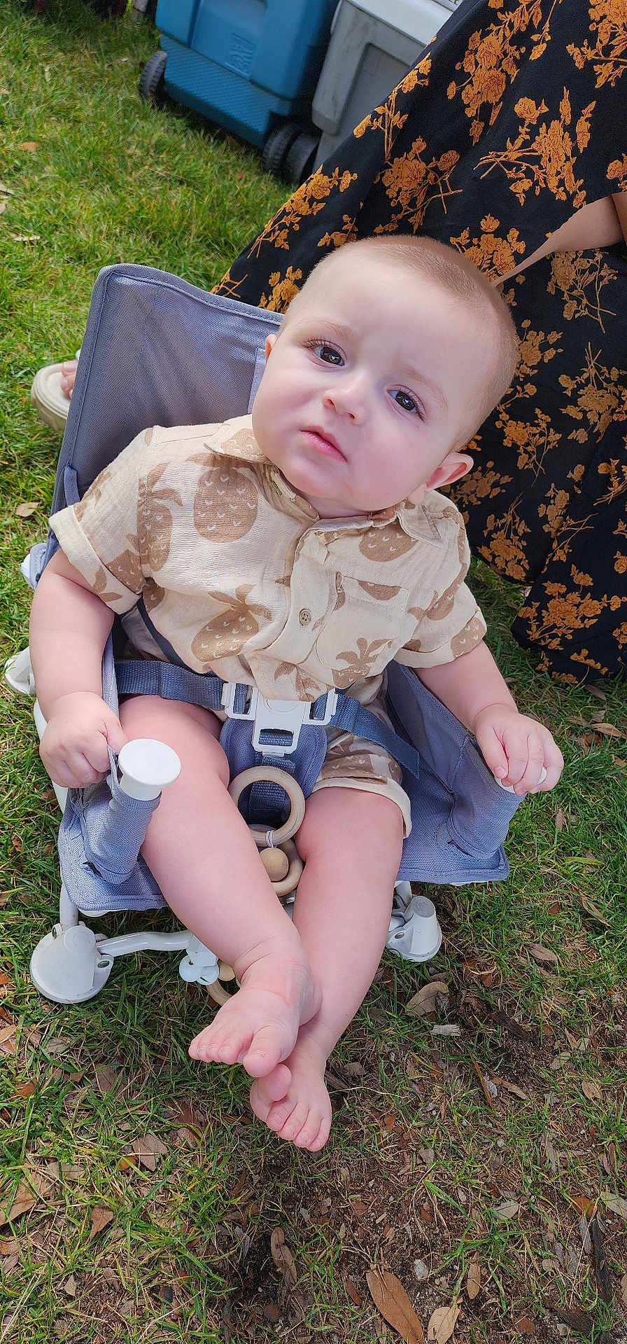 Rafael joined the competition — help win amazing prizes! baby, child, outdoor, grass, chair, clothing, pineapple_print, face, person, foot, hand, expression, seatbelt, summer, nature, skin, toy, fabric, pattern, footwear