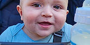 Rafael is registered to the contest to win money with this photo: baby, smiling, stroller, blue_blanket, bottle, milk_bottle, outdoor, child, happy, face, person, head, clothing, baby_clothes, infant, seatbelt, graco, nature, daylight, portrait