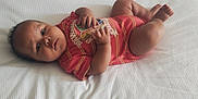 Prince Legend is registered to the contest to win money with this photo: baby, infant, onesie, red_clothing, striped, lying_down, blanket, texture, hand, legs, cute, child, portrait, skin, face, looking, young, indoors, resting, comfortable