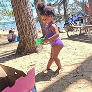 Trulia is registered to the contest to win money with this photo: toddler, child, purple_swimsuit, bubble_blower, beach, sand, trees, pine_trees, sunlight, shadows, box, training_pants, outdoor, play, summer, water, picnic_table, people, nature, daytime