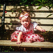 Haylee joined the competition — help win amazing prizes! baby, child, girl, pink_dress, bow, strawberry_pattern, bench, wooden_bench, outdoor, sunlight, shadow, greenery, leaves, curious, sitting, barefoot, portrait, daylight, nature, cute