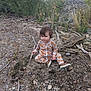 child, toddler, pajamas, fox_pattern, outdoor, nature, rocks, sticks, earth, grass, plants, shoes, dirt, sitting, curious, baby, person, exploring, casual_clothing, daylight