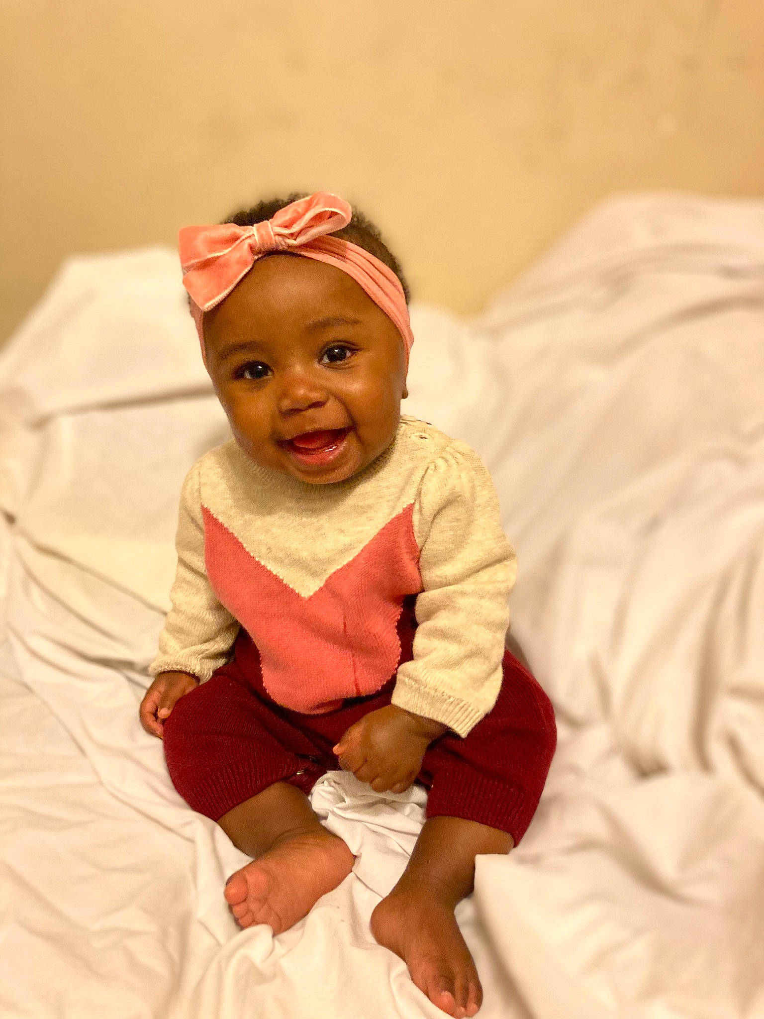 Leila is registered to the contest to win money with this photo: baby, baby_toddler_clothing, cap, carmine, child, comfort, costume_hat, event, fashion_accessory, fun, happy, hat, headwear, human_leg, linens, peach, person, room, sitting, sleeve