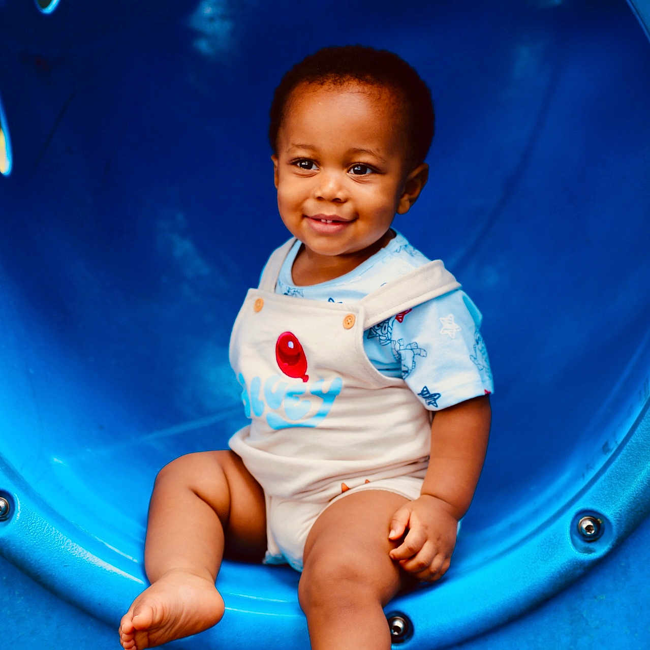 Jasiah joined the competition — help win amazing prizes! toddler, child, smiling, playground, blue_tunnel, romper, balloon_design, sitting, outdoor, happy, cute, baby, play, fun, park, person, clothing, feet, face, summer