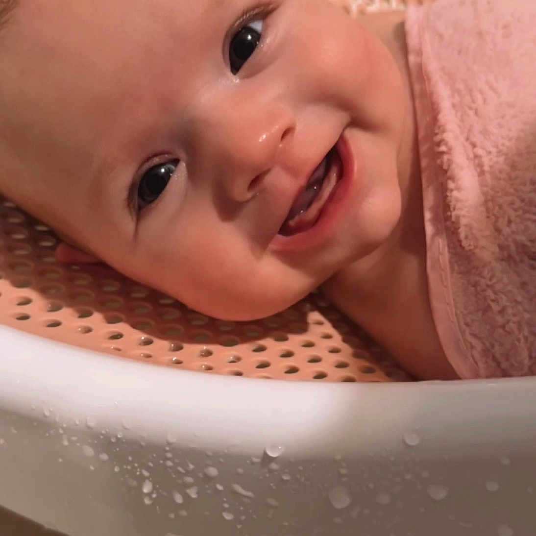 Josie joined the competition — help win amazing prizes! baby, infant, child, smiling, happy, portrait, face, eyes, teeth, bath, bath_seat, towel, pink, water_droplets, indoor, close_up, lying_down, warm_lighting, adorable, photography