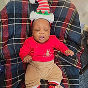 Kaiser joined the competition — help win amazing prizes! baby, celebration, child, christmas, cozy, cute, decorations, elf_hat, festive, footwear, hat, holiday, indoors, infant, plaid_blanket, portrait, red_clothing, sitting, smiling, sock