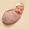 Gracie is registered to the contest to win money with this photo: newborn, baby, swaddled, sleeping, headband, flower, soft_fabric, portrait, indoor, closeup, peaceful, infant, skin, resting, cute, child, wrapped, beige_background, face, small