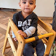 Angel joined the competition — help win amazing prizes! toddler, child, baby_chair, wooden_furniture, indoor, flooring, shirt, long_sleeves, pants, shoes, person, cute, sitting, young_child, face, expression, home, casual_clothing, curious, calm