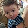 baby, infant, child, portrait, close_up, face, wide_eyed, curly_hair, messy_hair, striped_onesie, blue_clothing, sitting, indoor, home, sofa, couch, window, daylight, adult, family