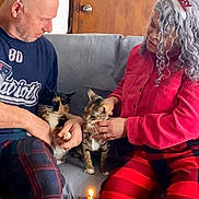 Lua And Tulipa is registered to the contest to win money with this photo: man, woman, cat, cats, couch, sofa, birthday_candle, candle, tin_can, party_hat, headband, plaid_pants, red_jacket, gray_hair, wooden_door, coffee_table, remote_control, sitting, petting, celebration