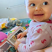 Soline participe au concours pour gagner de l'argent avec cette photo : baby, child, pajamas, photo_album, smile, face, hand, indoor, toy, furniture, curious, person, playtime, young_child, infant, home, sitting, looking_away, cute, cozy