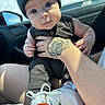baby, child, infant, beanie, hat, tattoo, hand, car_interior, window, shoe, sneaker, clothing, person, portrait, cute, holding, seat, daylight, face, curious