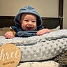 Lincoln joined the competition — help win amazing prizes! baby, smile, hood, blue_clothing, blanket, wooden_sign, bedroom, milestone, infant, cute, happy, face, pillow, bed, texture, hand, person, portrait, indoors, child