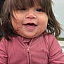 Madeline is registered to the contest to win money with this photo: child, toddler, baby, smiling, bangs, brown_hair, long_hair, zippered_jacket, pink_clothing, chubby_cheeks, dark_eyes, mouth, hand, close_up, portrait, indoor, stroller, seat, background_wall, happy