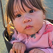 Madeline is registered to the contest to win money with this photo: child, toddler, baby, swing, playground, park, close_up, portrait, hands, eyes, bangs, pink_jacket, pink_clothing, sunlight, backlight, hair, expression, person, outdoors, play_equipment
