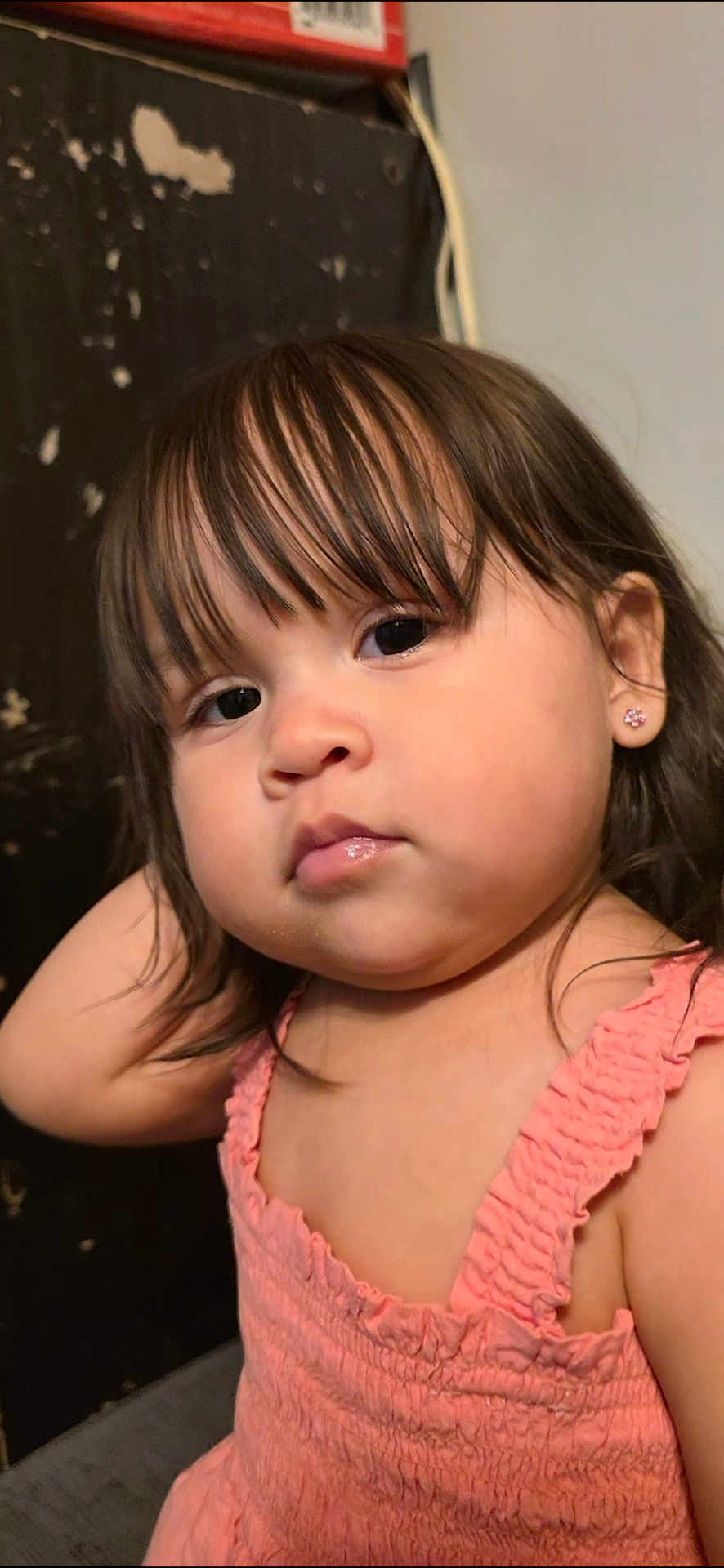 Madeline is registered to the contest to win money with this photo: toddler, child, girl, portrait, close_up, face, bangs, brown_hair, earring, pink_dress, sleeveless, chubby_cheeks, expressionless, eyes, lips, skin, indoor, candid, background_wall, young_child